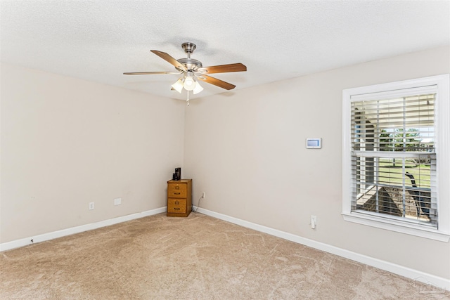 empty room with a textured ceiling, light colored carpet, baseboards, and ceiling fan