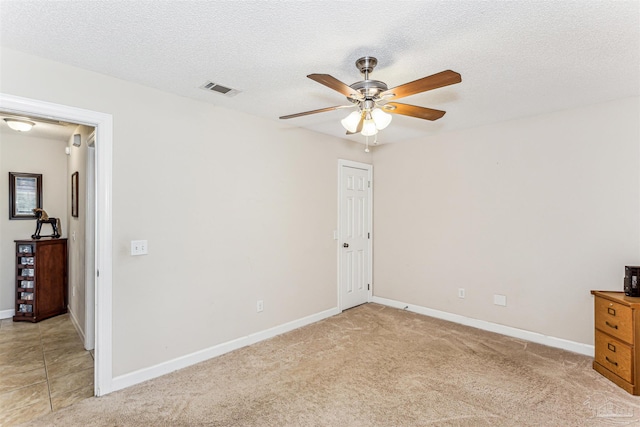 unfurnished bedroom featuring visible vents, a ceiling fan, a textured ceiling, baseboards, and light colored carpet
