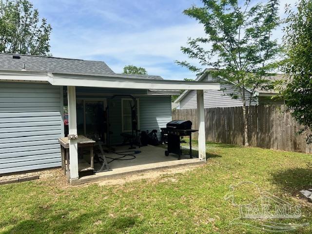 exterior space with a yard, a patio area, a shingled roof, and fence