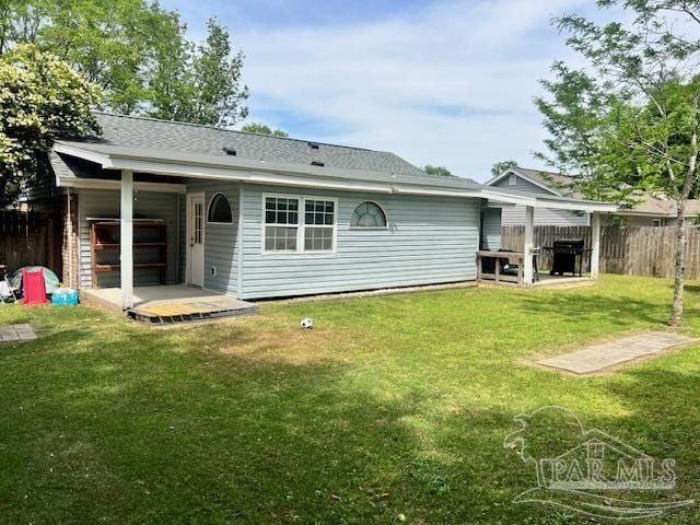 back of property featuring a yard, a shingled roof, and fence
