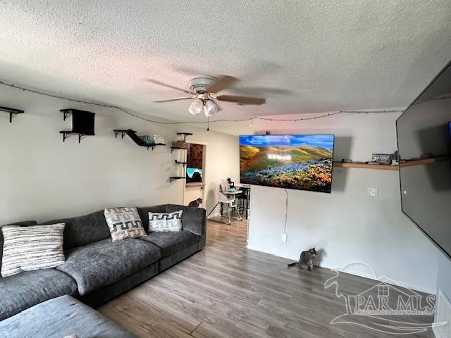 living area with wood finished floors, a textured ceiling, a ceiling fan, and baseboards
