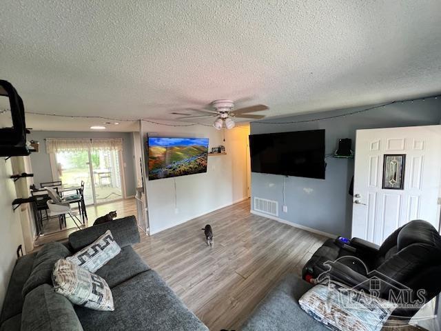living area with ceiling fan, a textured ceiling, and visible vents