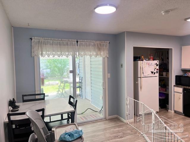 dining room featuring a textured ceiling, light wood finished floors, and baseboards