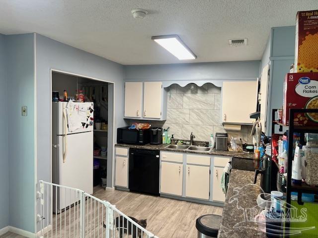 kitchen with white cabinets, light wood-style flooring, a sink, visible vents, and black appliances