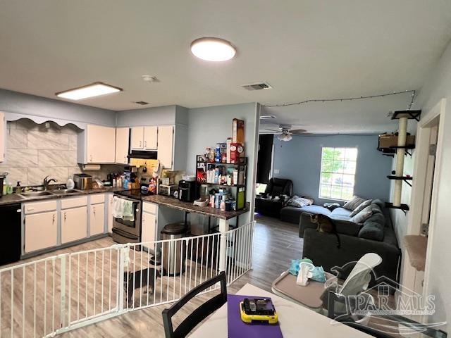 kitchen with white cabinets, dark countertops, visible vents, a sink, and stainless steel electric stove