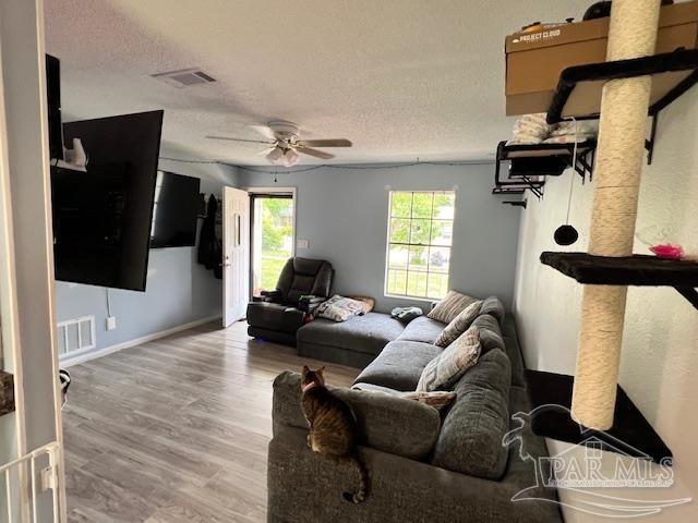 living room featuring wood finished floors, a ceiling fan, visible vents, and a textured ceiling