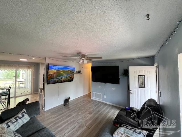 living area with a textured ceiling, baseboards, visible vents, wood finished floors, and ceiling fan
