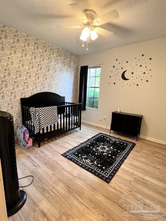 bedroom with light wood finished floors, wallpapered walls, baseboards, and a textured ceiling