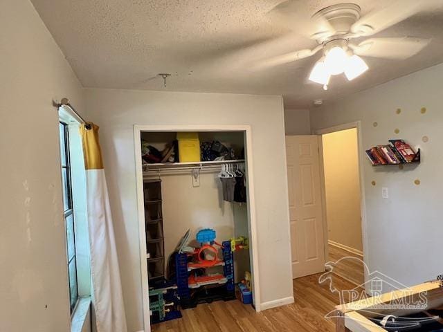 bedroom with a ceiling fan, wood finished floors, a textured ceiling, a closet, and baseboards