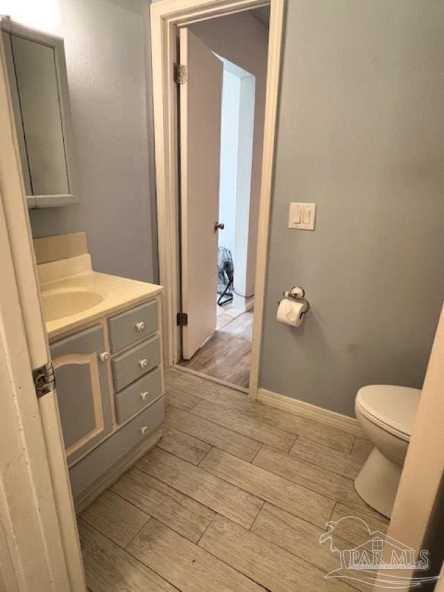 bathroom featuring baseboards, wood finished floors, vanity, and toilet