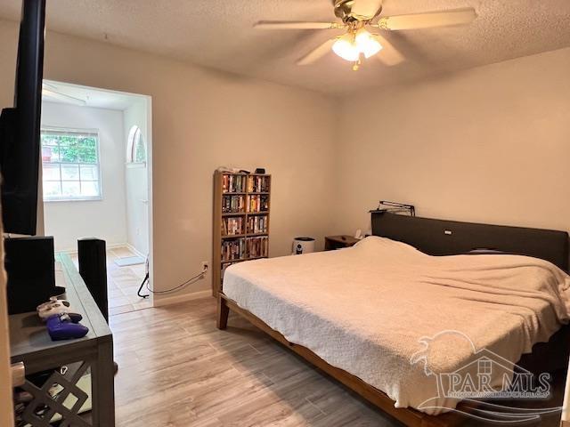 bedroom featuring baseboards, a textured ceiling, light wood-style floors, and ceiling fan