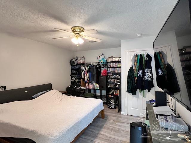 bedroom with a ceiling fan, wood finished floors, a textured ceiling, and a closet