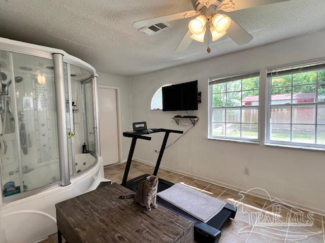 workout area featuring tile patterned floors, a textured ceiling, ceiling fan, baseboards, and visible vents