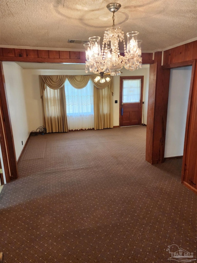 carpeted spare room with a textured ceiling, wood walls, and a notable chandelier