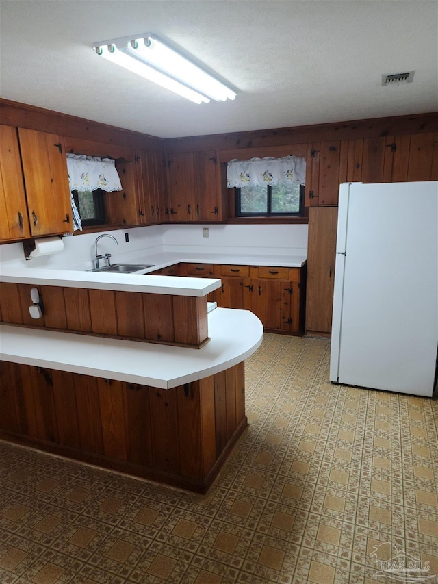 kitchen with a peninsula, freestanding refrigerator, a sink, light countertops, and tile patterned floors