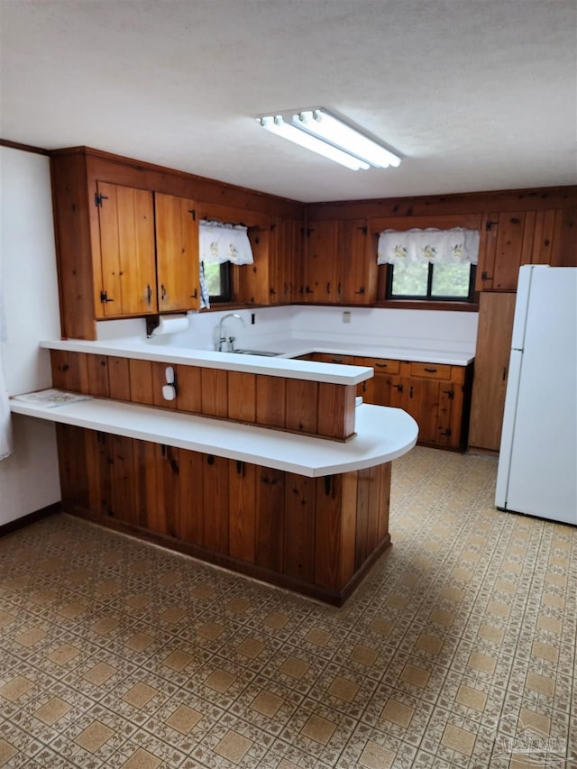 kitchen featuring white fridge, a breakfast bar area, kitchen peninsula, and sink