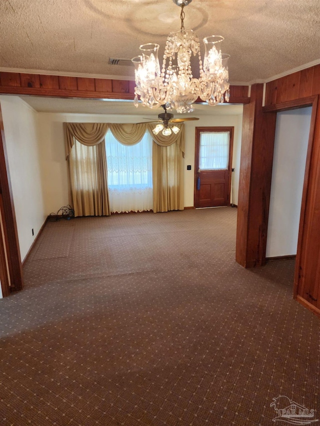 unfurnished room with an inviting chandelier, wooden walls, plenty of natural light, a textured ceiling, and carpet flooring