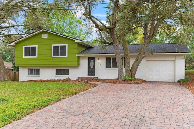 tri-level home featuring stucco siding, a garage, a front lawn, and decorative driveway