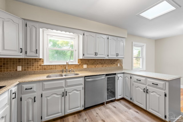 kitchen with a peninsula, light wood finished floors, dishwasher, wine cooler, and a sink