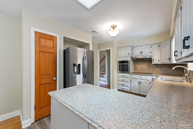kitchen with a sink, appliances with stainless steel finishes, a peninsula, visible vents, and decorative backsplash