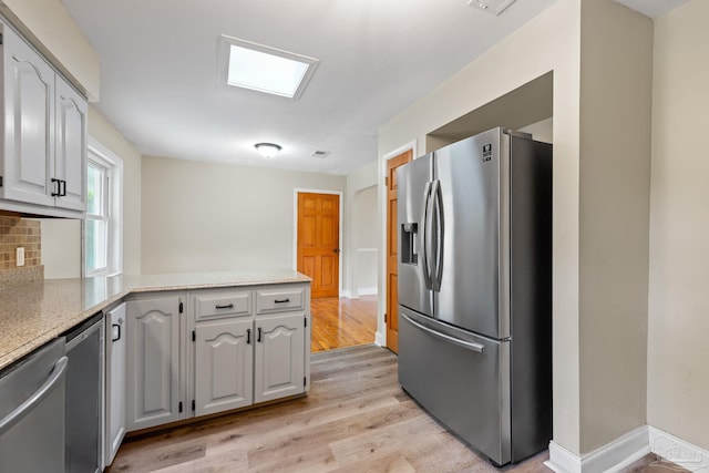 kitchen featuring stainless steel appliances, baseboards, backsplash, light wood finished floors, and a peninsula