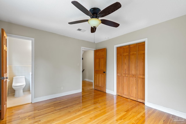unfurnished bedroom featuring tile walls, light wood-type flooring, ensuite bath, visible vents, and a closet