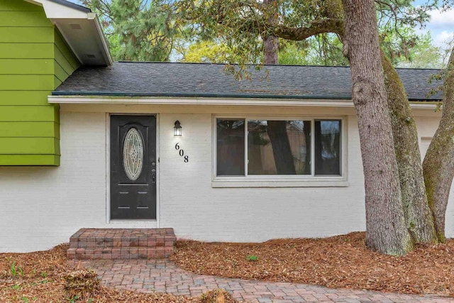 doorway to property featuring brick siding and roof with shingles
