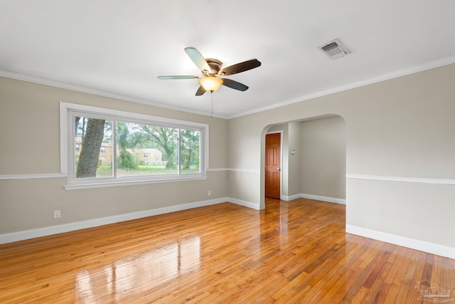 unfurnished room featuring crown molding, light wood finished floors, baseboards, arched walkways, and ceiling fan
