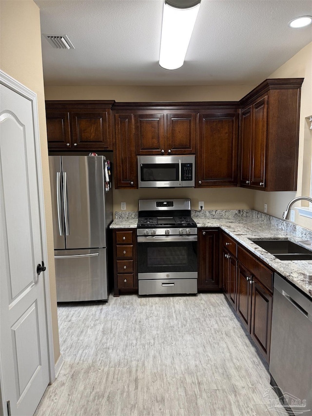 kitchen featuring light stone countertops, appliances with stainless steel finishes, sink, and dark brown cabinetry