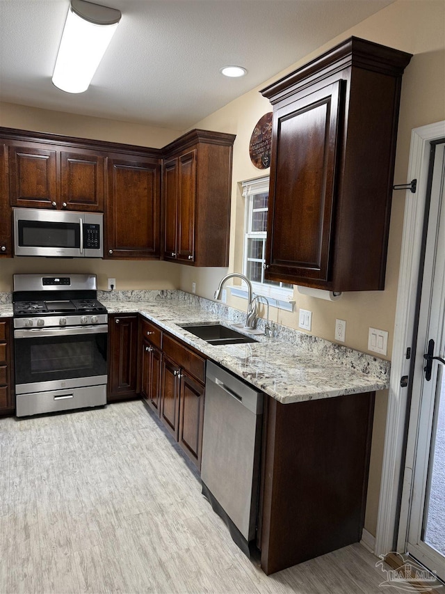 kitchen featuring dark brown cabinetry, sink, light stone counters, and appliances with stainless steel finishes