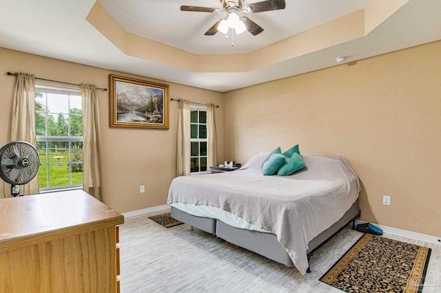 bedroom featuring ceiling fan, light hardwood / wood-style floors, and a tray ceiling