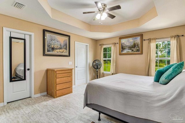 carpeted bedroom with ceiling fan, a tray ceiling, and multiple windows