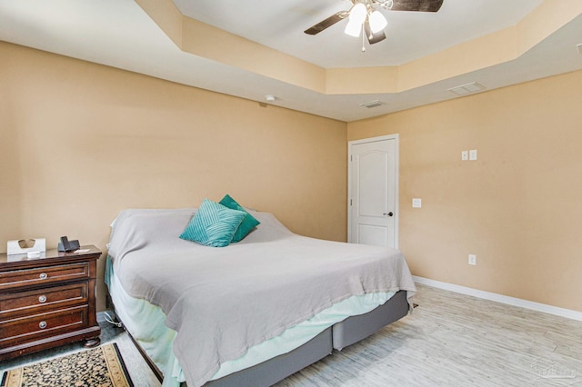 bedroom with ceiling fan, light wood-type flooring, and a tray ceiling