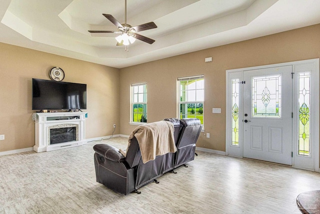 living room featuring a tray ceiling, ceiling fan, and light wood-type flooring