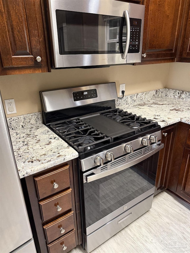 kitchen with light stone counters, dark brown cabinetry, and stainless steel appliances