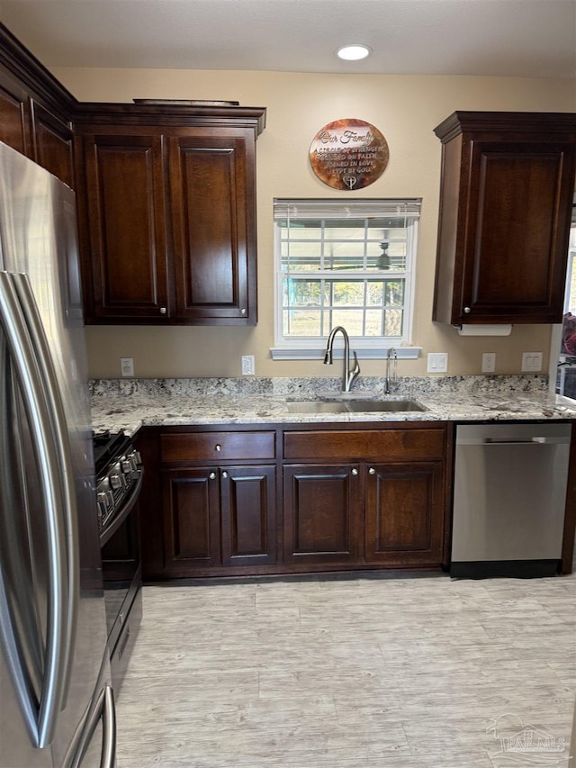 kitchen featuring stainless steel appliances, light stone countertops, sink, and dark brown cabinets