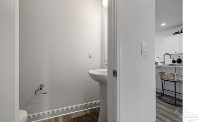 bathroom featuring crown molding, baseboards, wood finished floors, toilet, and a sink