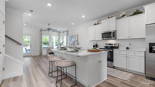 kitchen featuring visible vents, crown molding, a kitchen island with sink, a kitchen bar, and appliances with stainless steel finishes