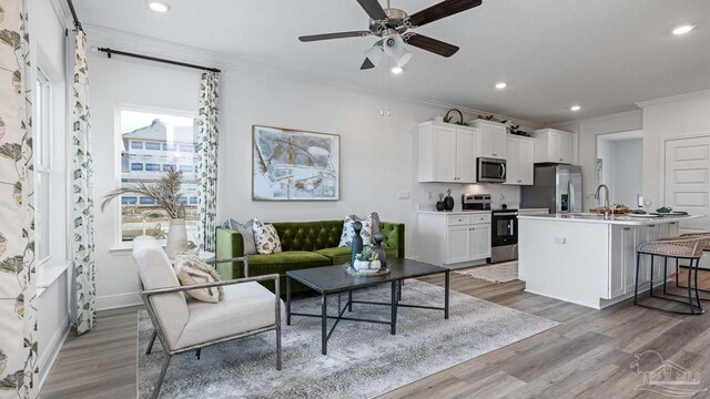 living area featuring recessed lighting, light wood-type flooring, ornamental molding, baseboards, and a ceiling fan