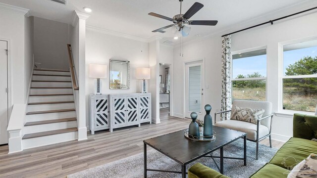 living area with stairs, wood finished floors, baseboards, ceiling fan, and ornamental molding