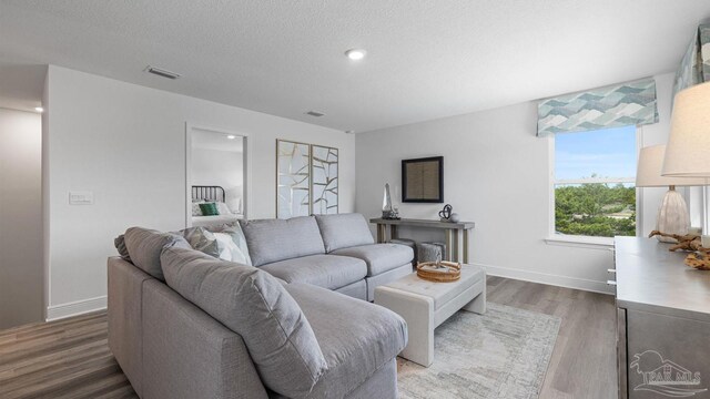 living room featuring baseboards, visible vents, a textured ceiling, and wood finished floors