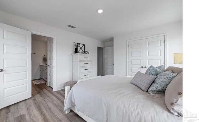 bedroom featuring a closet, visible vents, baseboards, connected bathroom, and wood finished floors