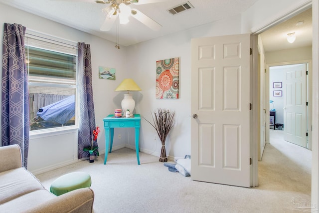 sitting room with light carpet, a textured ceiling, and ceiling fan