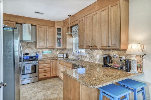 kitchen featuring light stone counters, a peninsula, a sink, appliances with stainless steel finishes, and wall chimney range hood