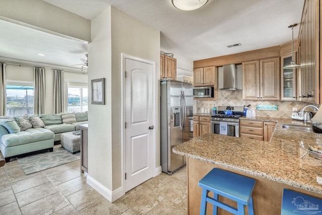 kitchen with a sink, wall chimney exhaust hood, light stone countertops, and stainless steel appliances