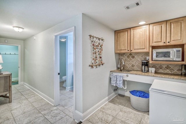 kitchen with visible vents, a sink, backsplash, baseboards, and light stone countertops