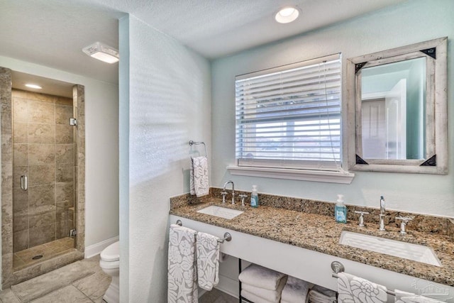 bathroom with a sink, toilet, a stall shower, and double vanity