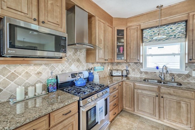 kitchen with light stone countertops, a sink, decorative backsplash, stainless steel appliances, and wall chimney exhaust hood