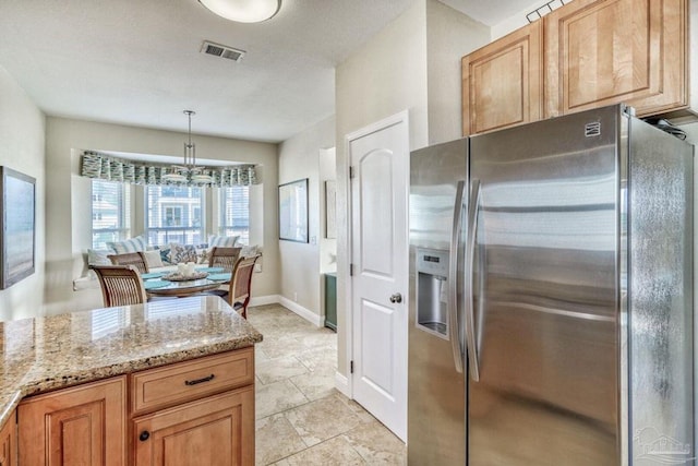 kitchen with visible vents, pendant lighting, stainless steel fridge, baseboards, and light stone countertops