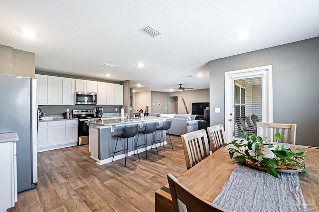 kitchen featuring white cabinetry, a kitchen breakfast bar, light hardwood / wood-style flooring, a kitchen island with sink, and appliances with stainless steel finishes